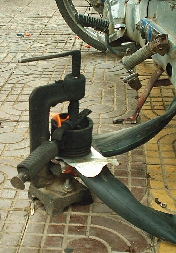 An upside motorcycle piston and C-clamp on a tire tube with a small fire to  seal a hole during Phnom Penh Diary 2007.